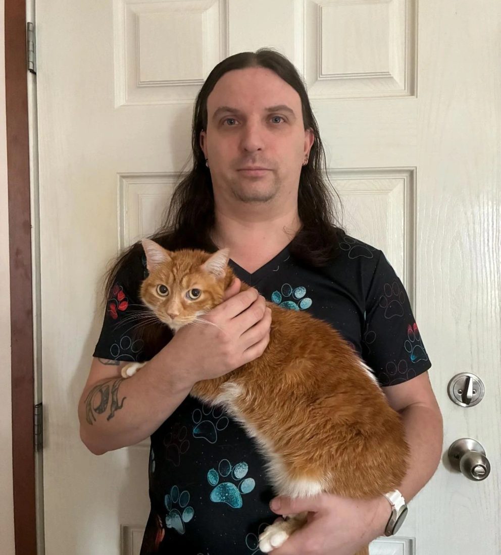Man with long hair holding an orange cat in front of a white door