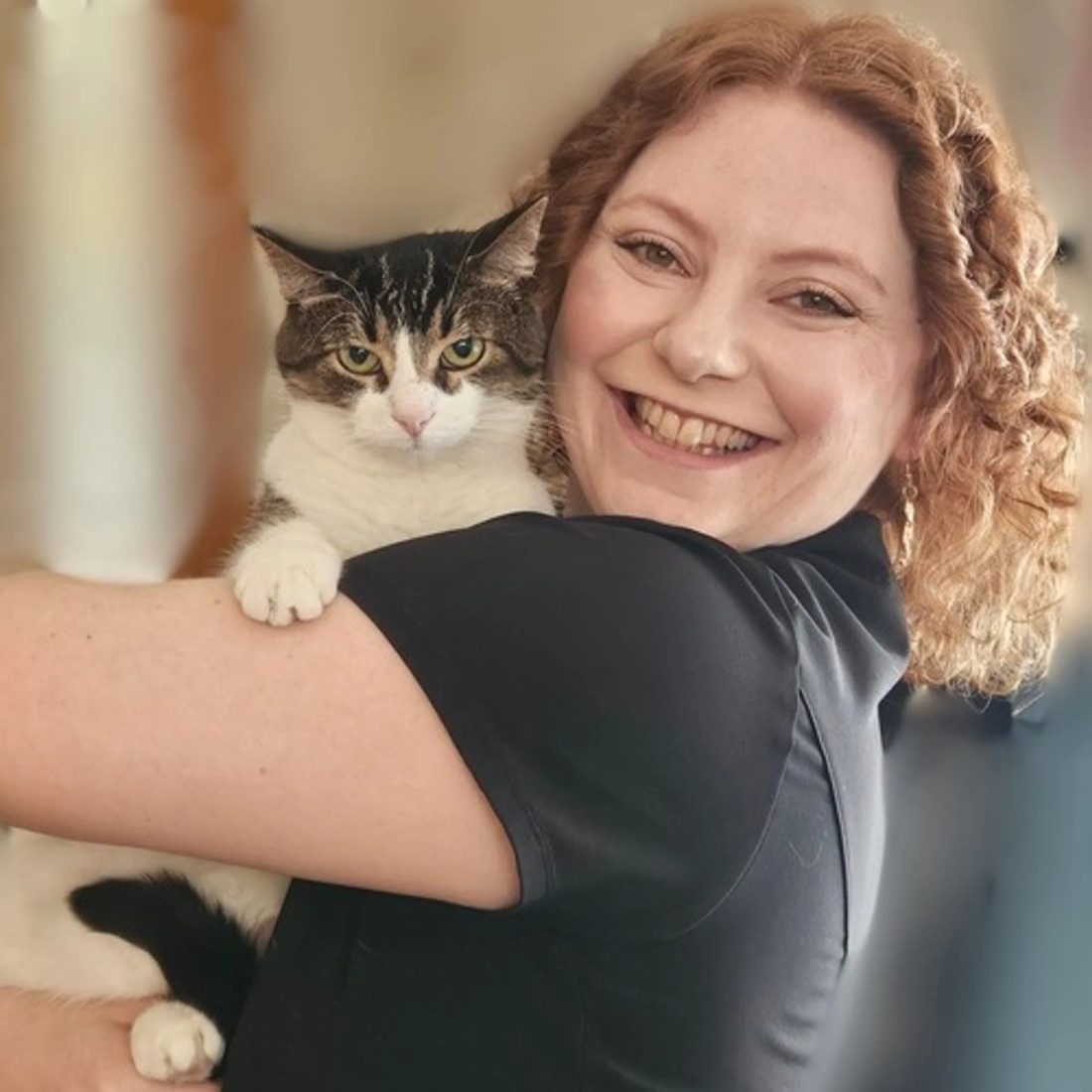 Smiling woman with curly hair holding a tabby cat
