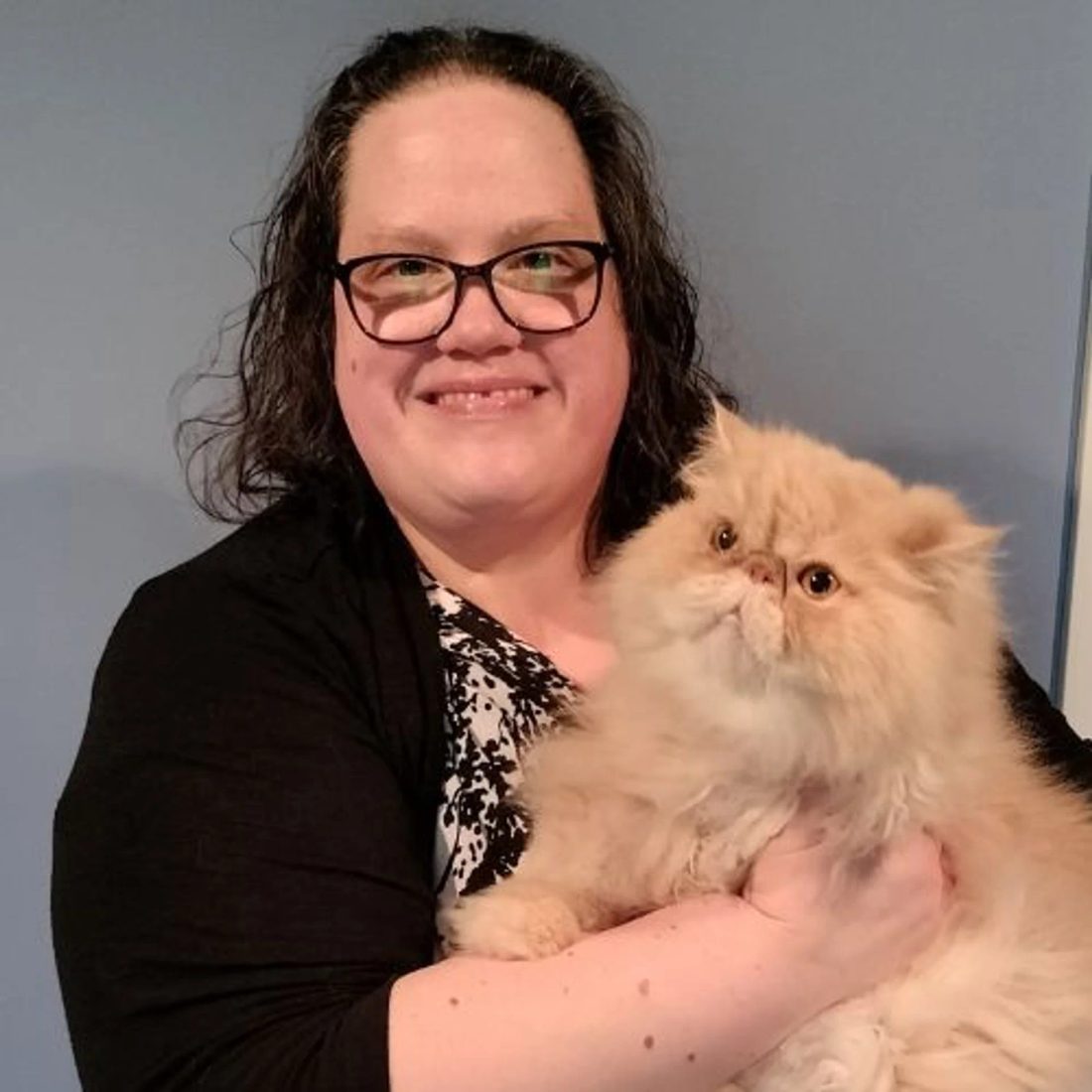 Smiling woman with glasses holding a fluffy orange cat