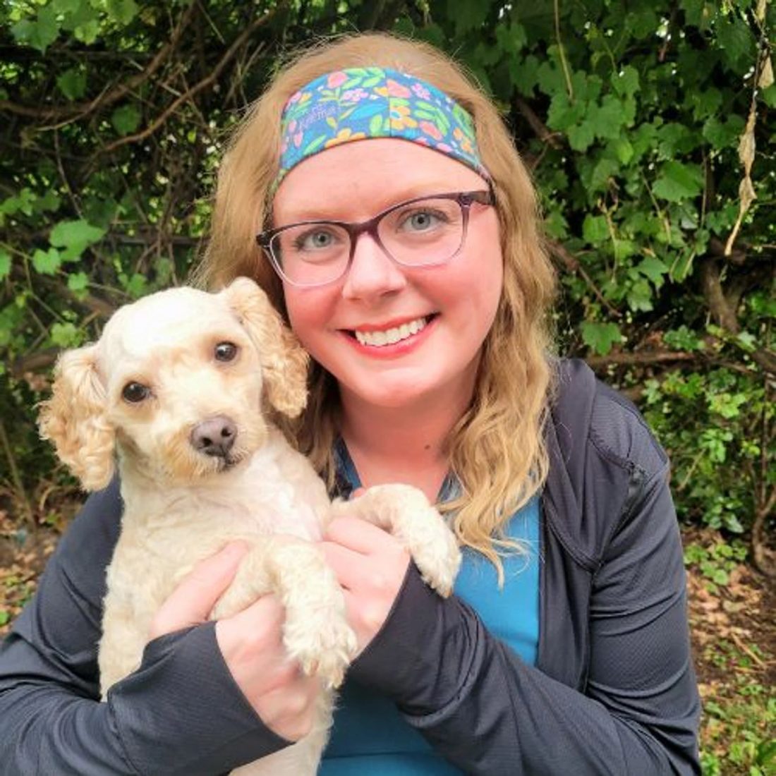 Woman with glasses and headband holding a small white dog outdoors